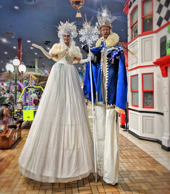 Ice King and Snow Queen stilt-walkers in sparkling winter costumes at indoor event