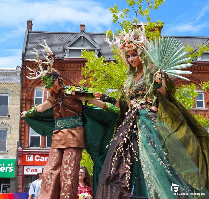 Enchanted forest stilt-walkers with antler headpieces on city street
