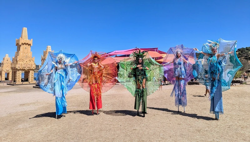 Five elemental stilt-walkers with dramatic wing costumes at festival