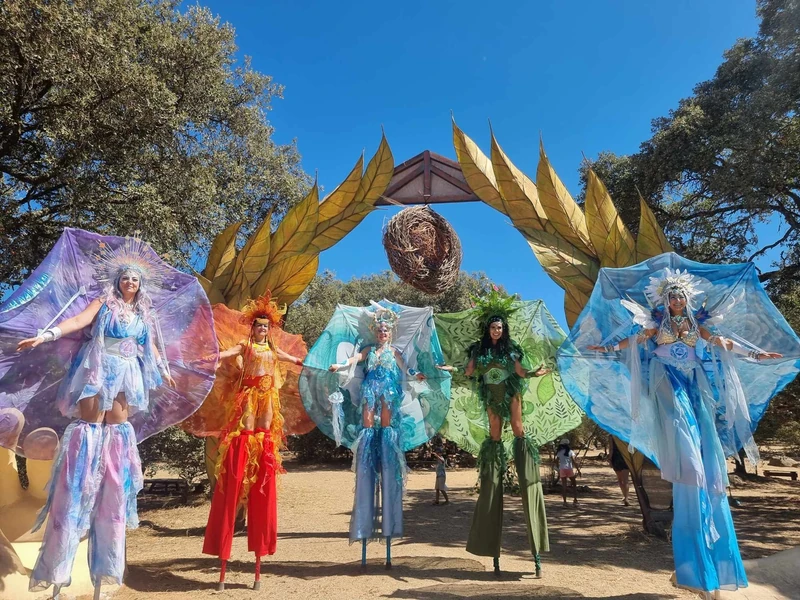 Five elemental stilt-walkers under golden arch at festival
