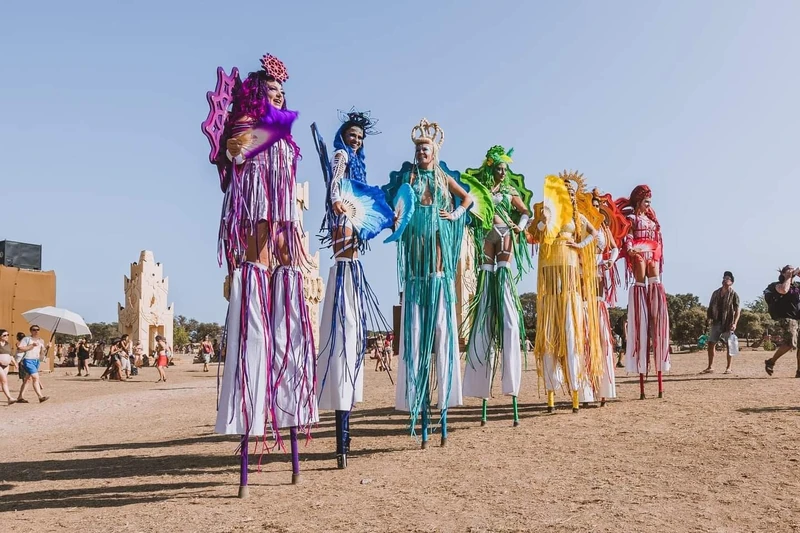 Rainbow line of stilt-walkers in coordinated festival costumes