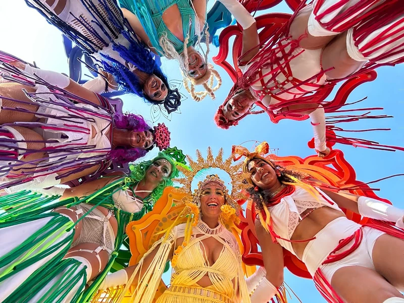 Looking up at a circle of rainbow stilt-walkers with colourful headpieces against blue sky