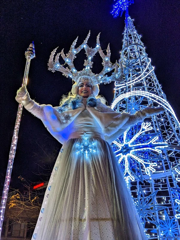 Ice queen stilt-walker with LED crystal antler crown beside illuminated Christmas tree installation