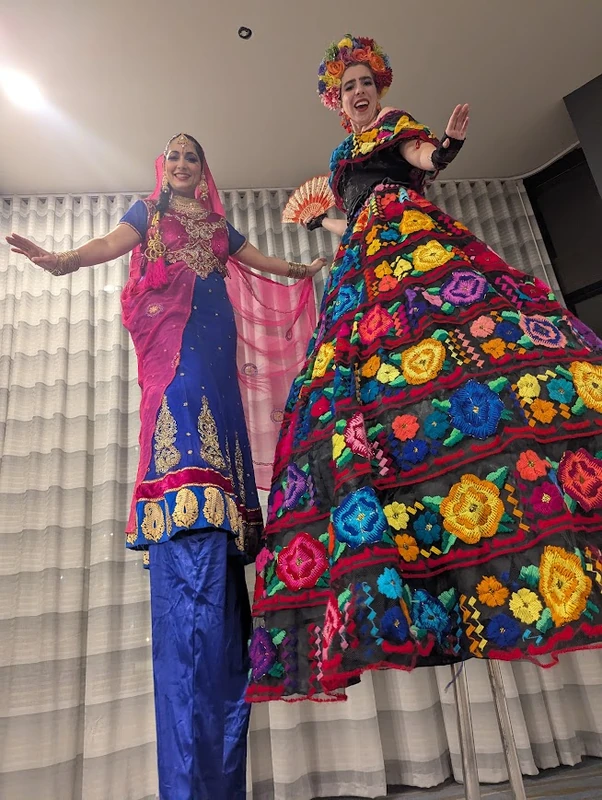 Bollywood and Mexican folk stilt-walkers in vibrant traditional costumes at indoor event