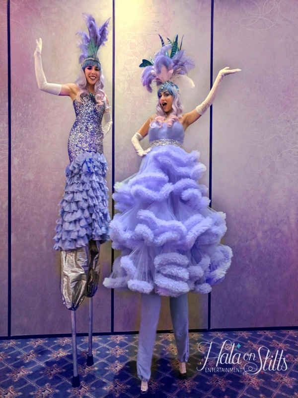 Two lavender and purple tulle-dressed stilt-walkers with feathered headpieces at elegant event