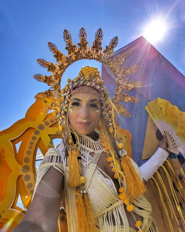 Golden sun goddess stilt performer with ornate crown and macrame costume at festival