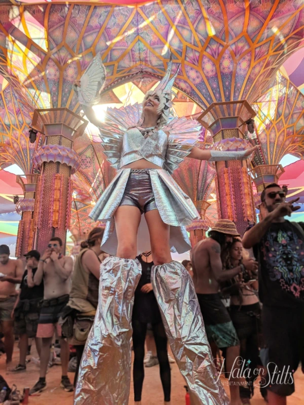 Silver futuristic angel stilt-walker with metallic wings at psychedelic festival stage