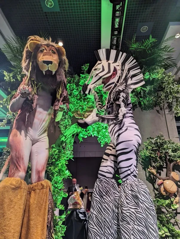 Safari lion and zebra stilt-walkers in realistic animal costumes at indoor jungle event