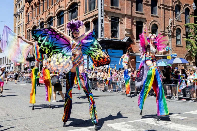 Three rainbow butterfly stilt-walkers marching in Toronto Pride Parade with massive crowds along Yonge Street