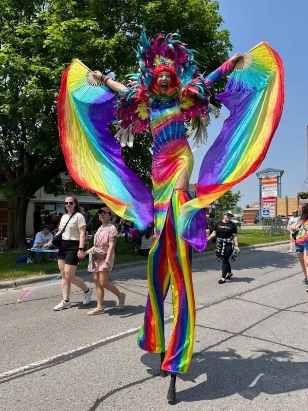 Rainbow feathered Pride stilt-walker with flowing silk fans performing at suburban Pride parade