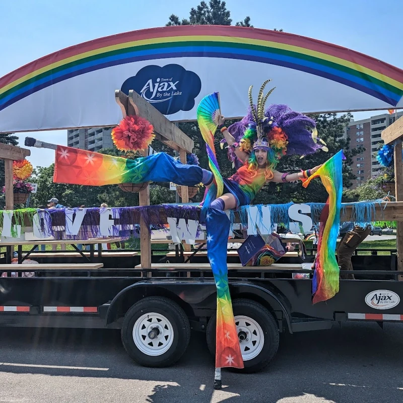 Rainbow stilt performer doing high kick beside Ajax Pride parade float with Love Wins banner