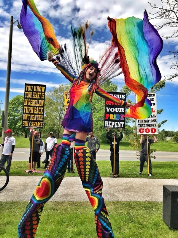 Rainbow Pride stilt performer standing defiantly tall with flowing fans at community Pride event