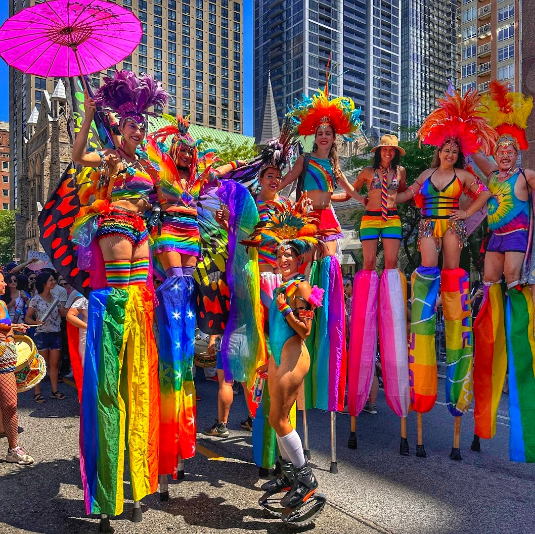 Large team of Pride stilt-walkers in various rainbow costumes marching together at Toronto Pride