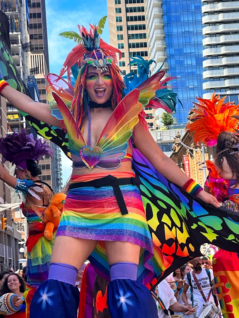 Pride parade stilt-walkers in vivid rainbow costumes performing for cheering crowd at street festival