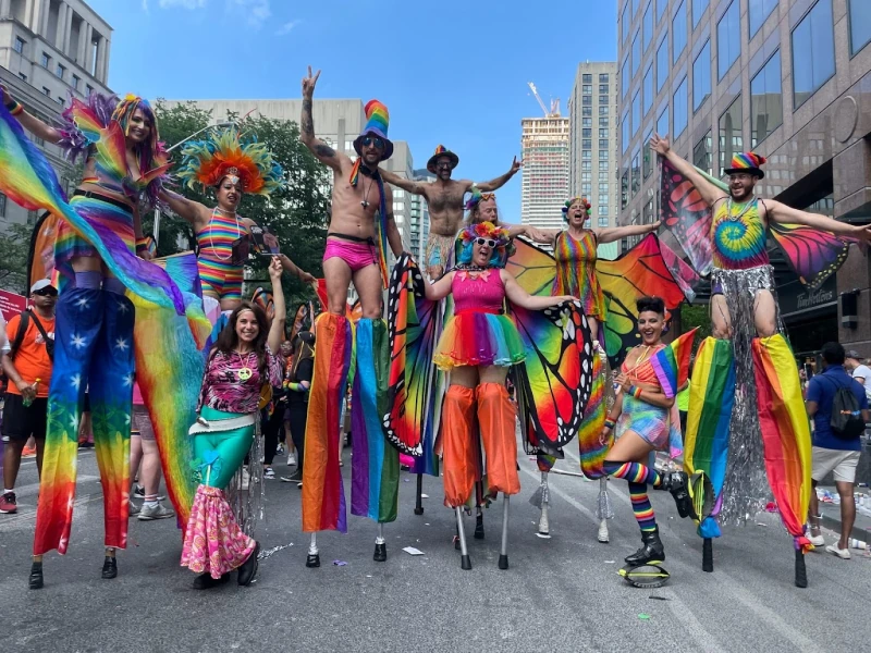 Full team of rainbow stilt performers at large outdoor Pride festival with colourful costumes and fans