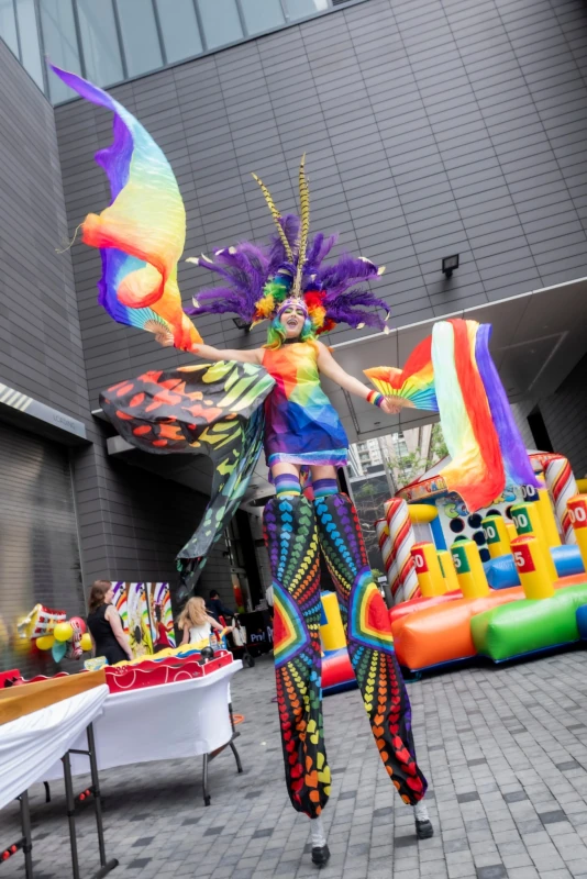 Pride stilt performer with purple headdress and butterfly wings at corporate indoor event