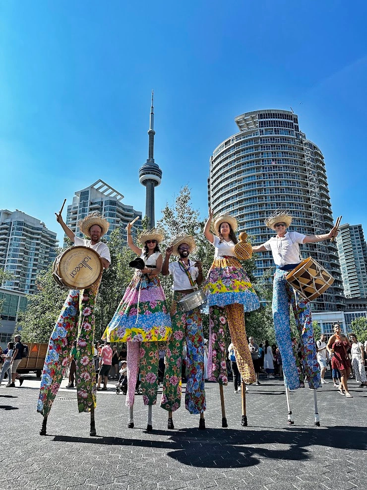 Six TallBeat stilt-walkers posing in front of the CN Tower in Toronto with drums raised overhead